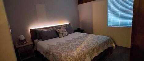 A bedroom with a bed, bedside table, and a window with blinds.