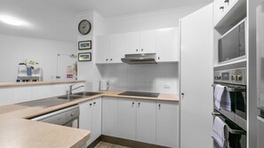 A modern kitchen with white cabinetry, a stainless steel sink, a built-in oven, and a microwave. - Sanctuary Lake Apartment 25 - Peaceful Beachside Currumbin - Min. 3 Nights - Linen Provided (Currumbin)