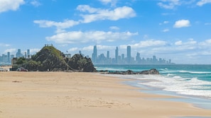 Ein Strand mit einem Felsen und einer Stadtansicht im Hintergrund.