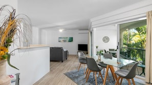A modern living space with a dining area, a sofa, a TV, and a balcony with plants. - Sanctuary Lake Apartment 25 - Peaceful Beachside Currumbin - Min. 3 Nights - Linen Provided (Currumbin)