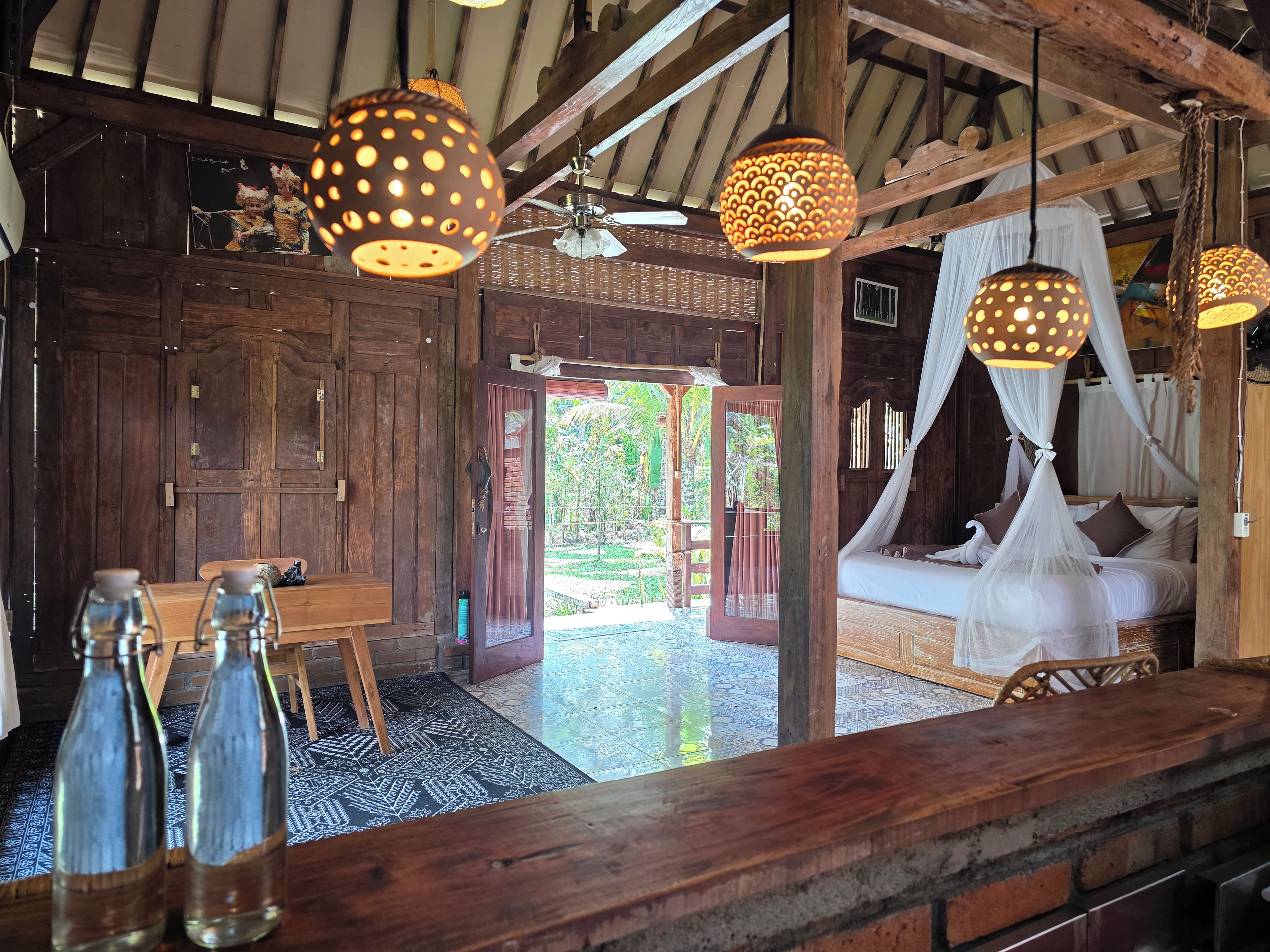 A rustic wooden room with a bed, hanging lamps, and a view of the outdoors.