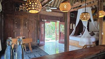 A rustic wooden room with a bed, hanging lamps, and a view of the outdoors.