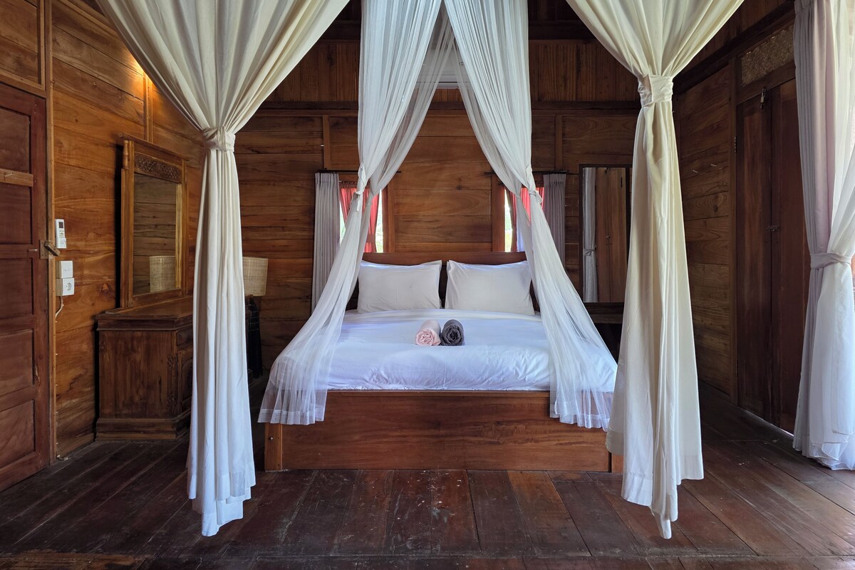 Una camera in legno con un letto a baldacchino, tende e uno specchio.