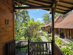 A wooden veranda with a view of a garden and a traditional building with a tiled roof.