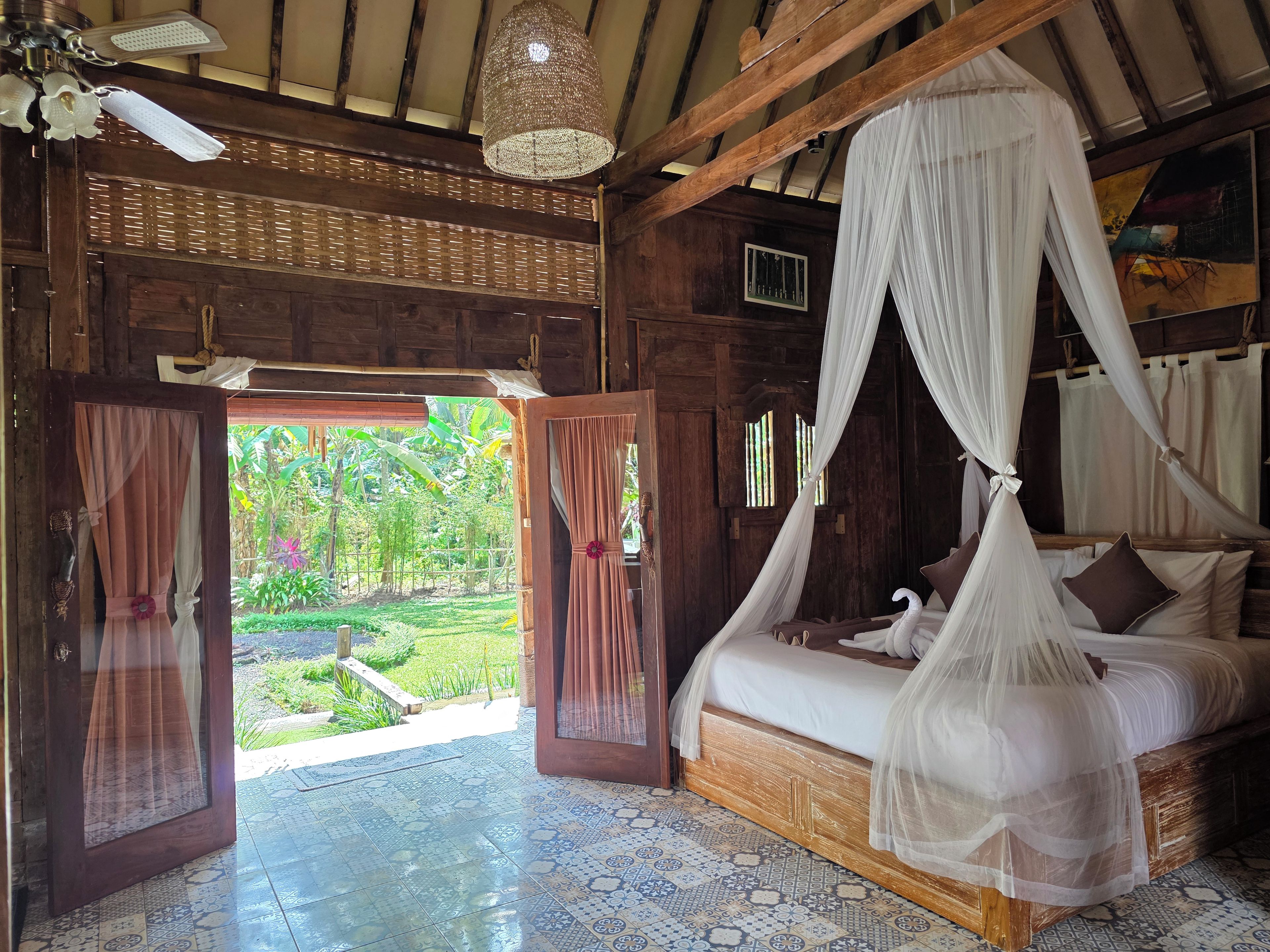 A room with a bed under a canopy, wooden walls, and a view of greenery outside.