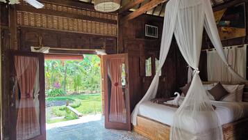 A room with a bed under a canopy, wooden walls, and a view of greenery outside.