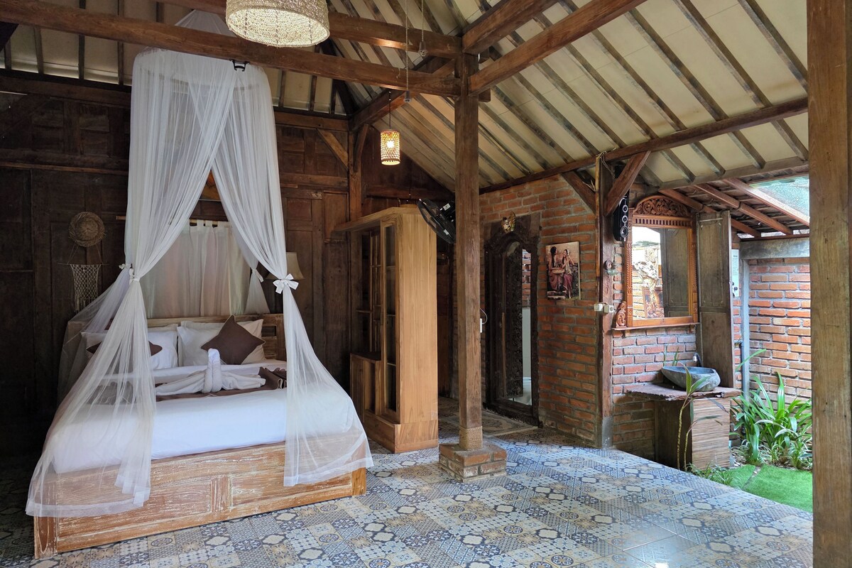 A room with a four-poster bed, a wooden ceiling, and patterned floor tiles.
