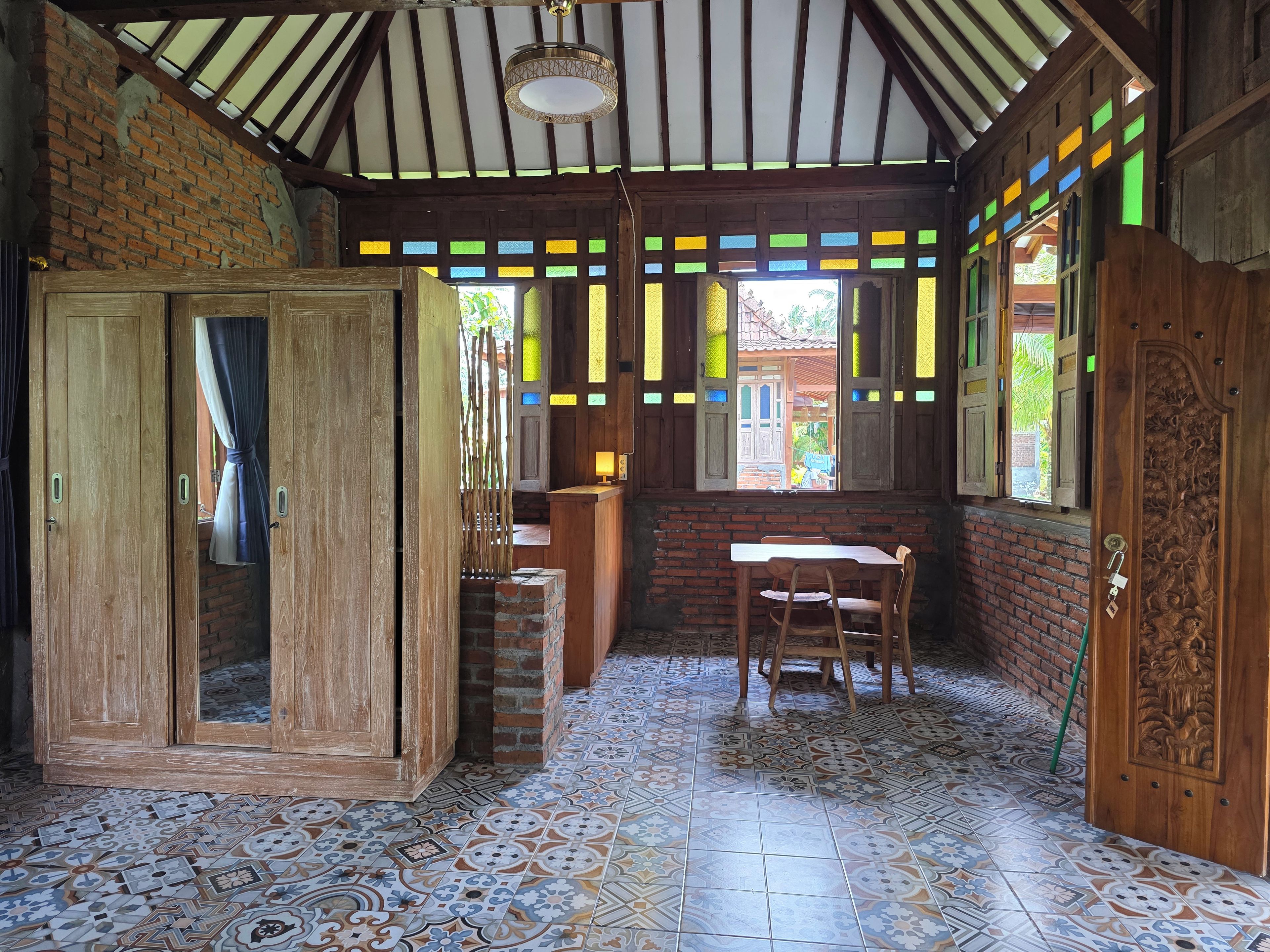 Una habitación con suelo de baldosas, muebles de madera, una puerta de madera con intrincados grabados y un ventanal con vidrieras de colores.