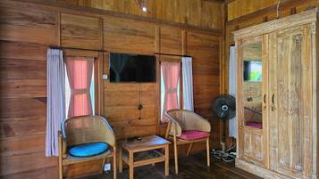 Een kamer met houten vloeren, twee rieten stoelen, een tafeltje, een televisie en een kledingkast.
