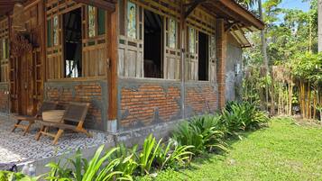 A traditional wooden house with a porch, a tiled floor, and a garden with plants.