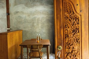 Een houten tafel met twee glazen flessen en een klein oranje voorwerp, een stoel en een kast tegen een structuurrijke muur.