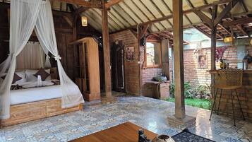 A room with a bed under a canopy, a wooden table with a vase and remote, and a brick wall with a door.