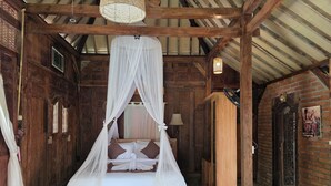 A wooden room with a bed under a canopy, a fan, and a patterned floor.
