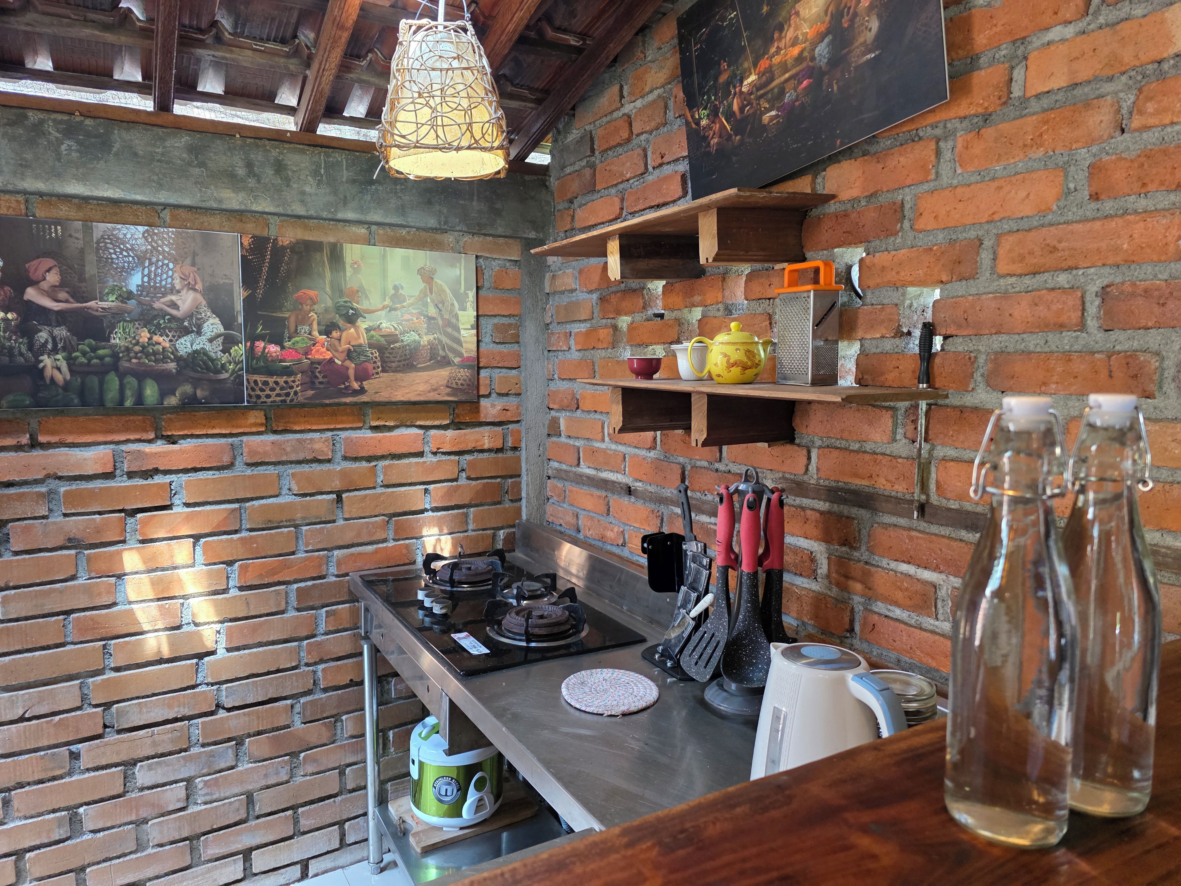 Une cuisine aux murs en briques, dotée d’un luminaire suspendu et d’une étagère où sont rangés les ustensiles de cuisine.
