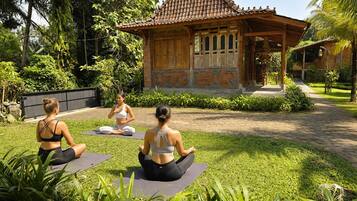 Three individuals meditating on yoga mats in a garden with a traditional wooden structure in the background.