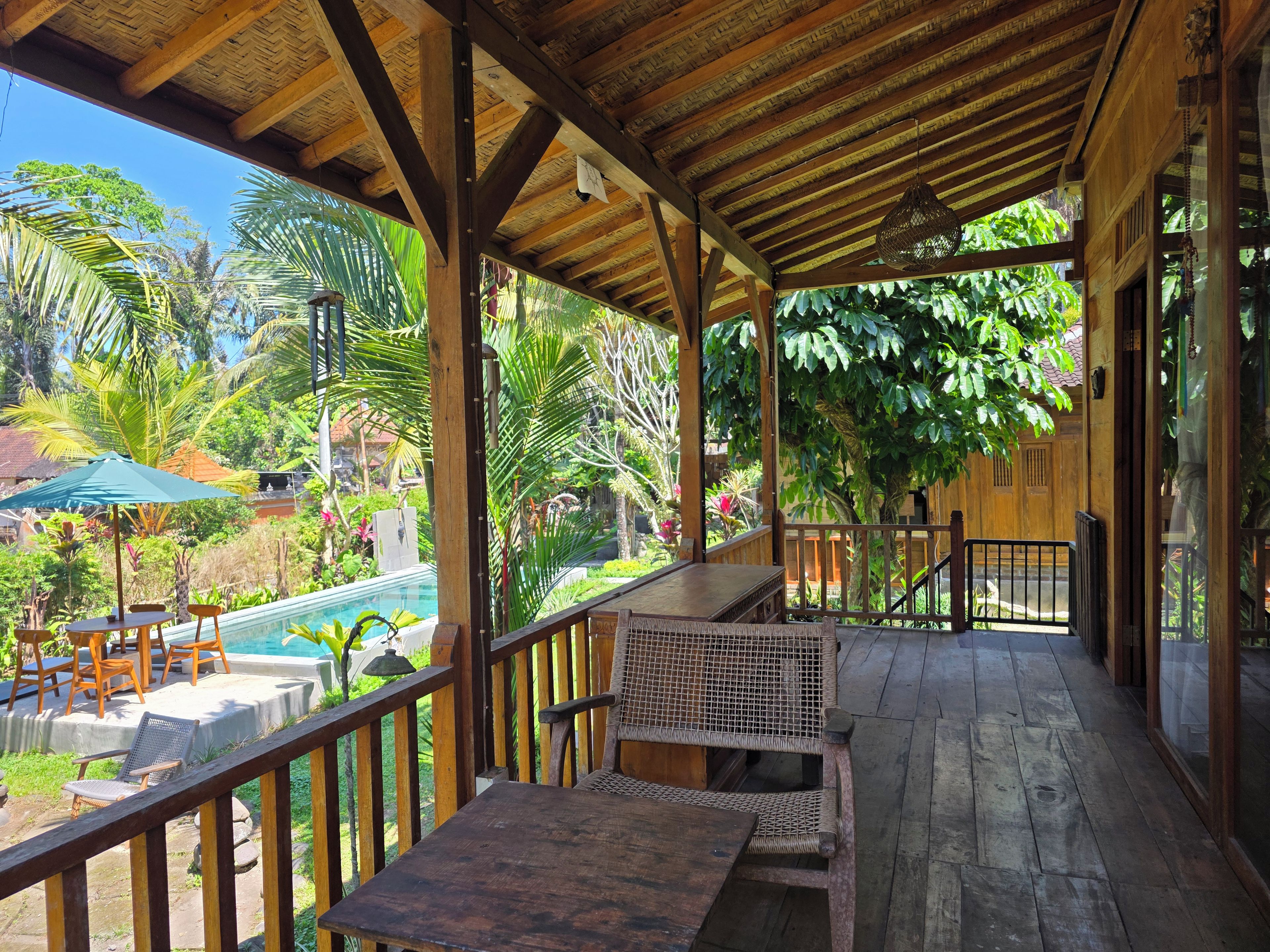 A covered outdoor area with a pool, wooden furniture, and lush greenery.