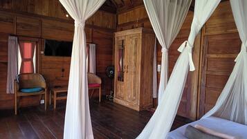 Ein Zimmer in einer Holzhütte mit einem Bett, einem Sessel, einem Ventilator und einem Kleiderschrank.