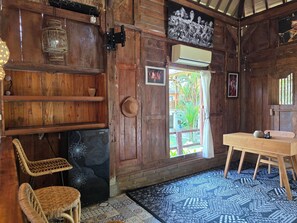A wooden room with a wooden table, two wicker chairs, a patterned rug, a door with a view to the outside, and a wall-mounted air conditioner. - Sangeh Lodge (Abiansemal)