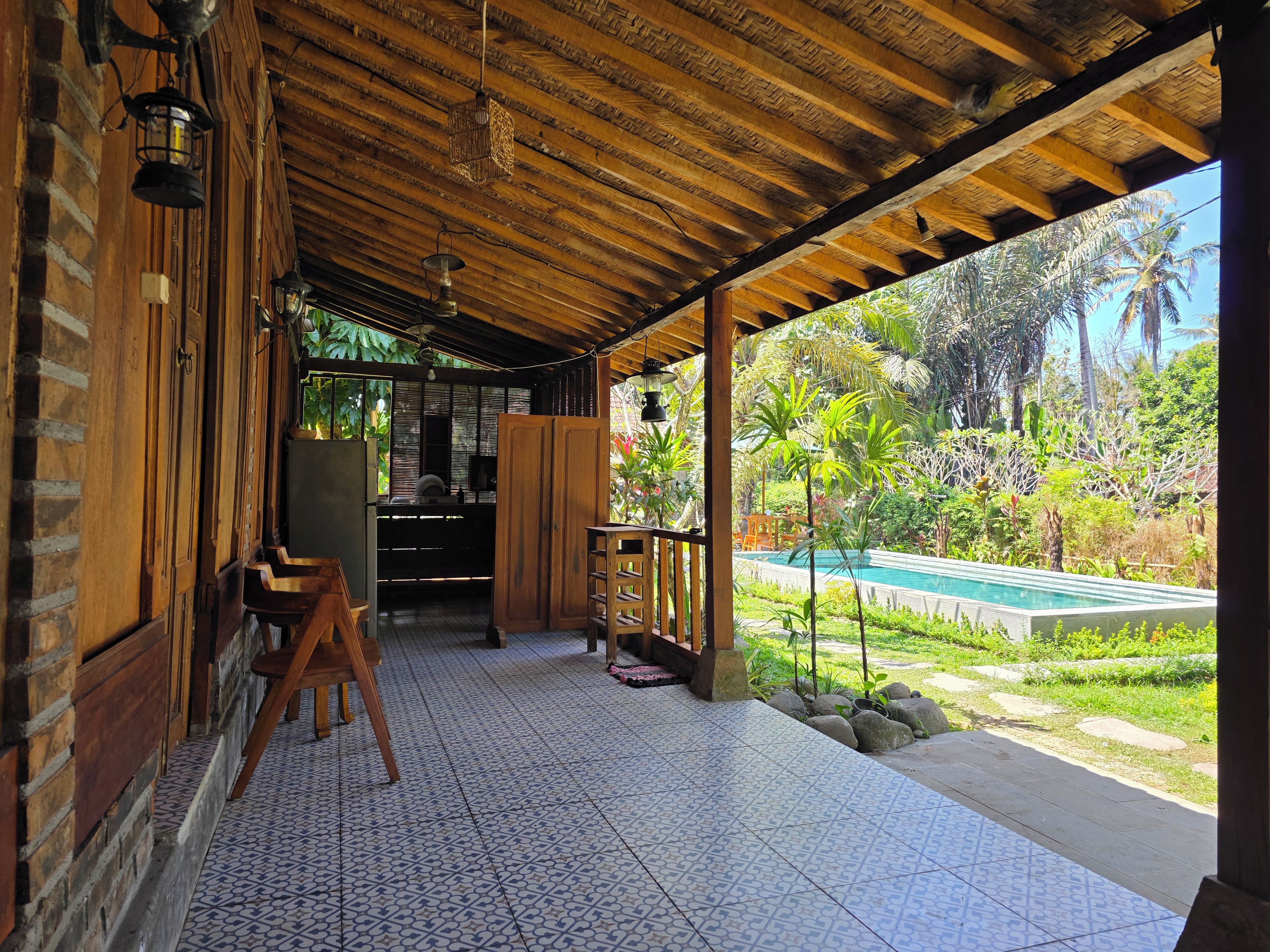 A covered outdoor area with a tiled floor, wooden furniture, and a view of a swimming pool.