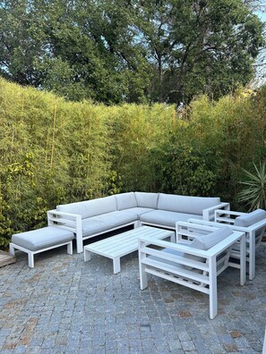 A white outdoor seating area with a sofa, benches, and tables, surrounded by dense greenery. - A Beautiful House in Les Restanques (Grimaud)
