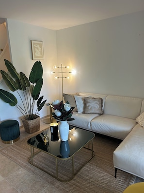 A modern living room with a sofa, a coffee table with a vase, a floor lamp, and large green plants. - A Beautiful House in Les Restanques (Grimaud)