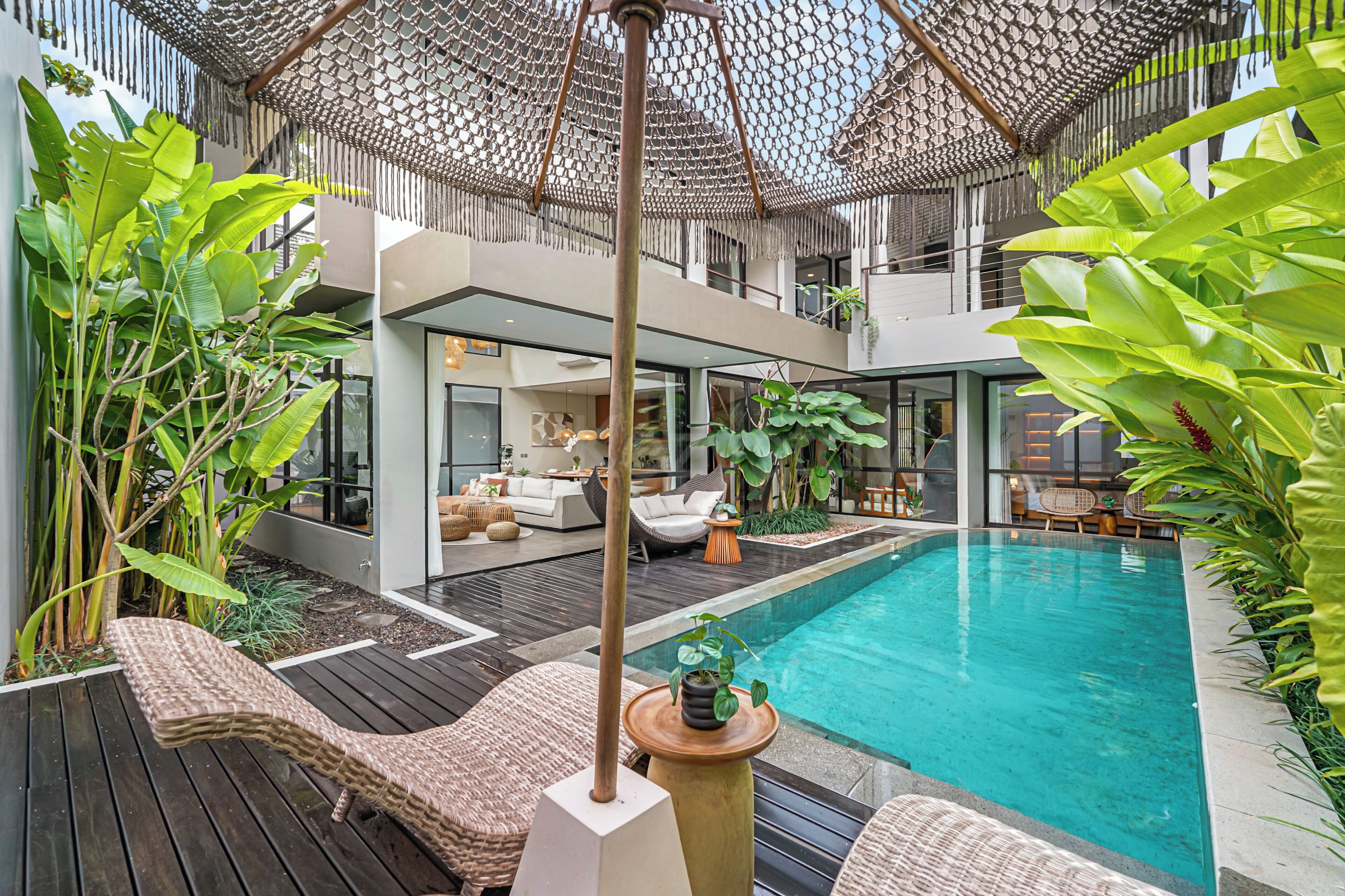 A modern outdoor pool area with a wooden deck, lounge chairs, and a hanging umbrella.