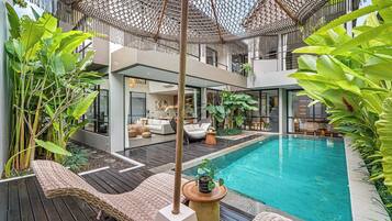 A modern outdoor pool area with a wooden deck, lounge chairs, and a hanging umbrella.