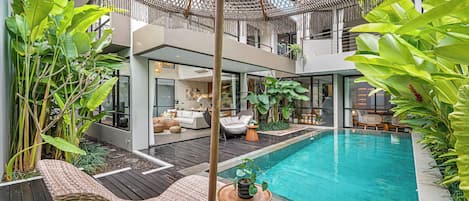 Un área de piscina exterior moderna con cubierta de madera, sillones de descanso y una sombrilla colgante.