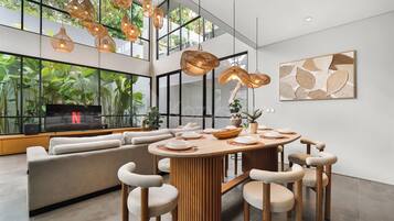 A modern living room with a large window, a dining area with a round table, and a sofa.