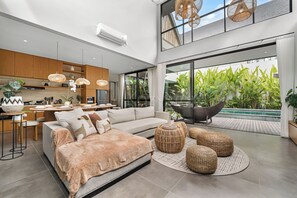 A modern living space with a large sofa, a dining area, and a view of a swimming pool.