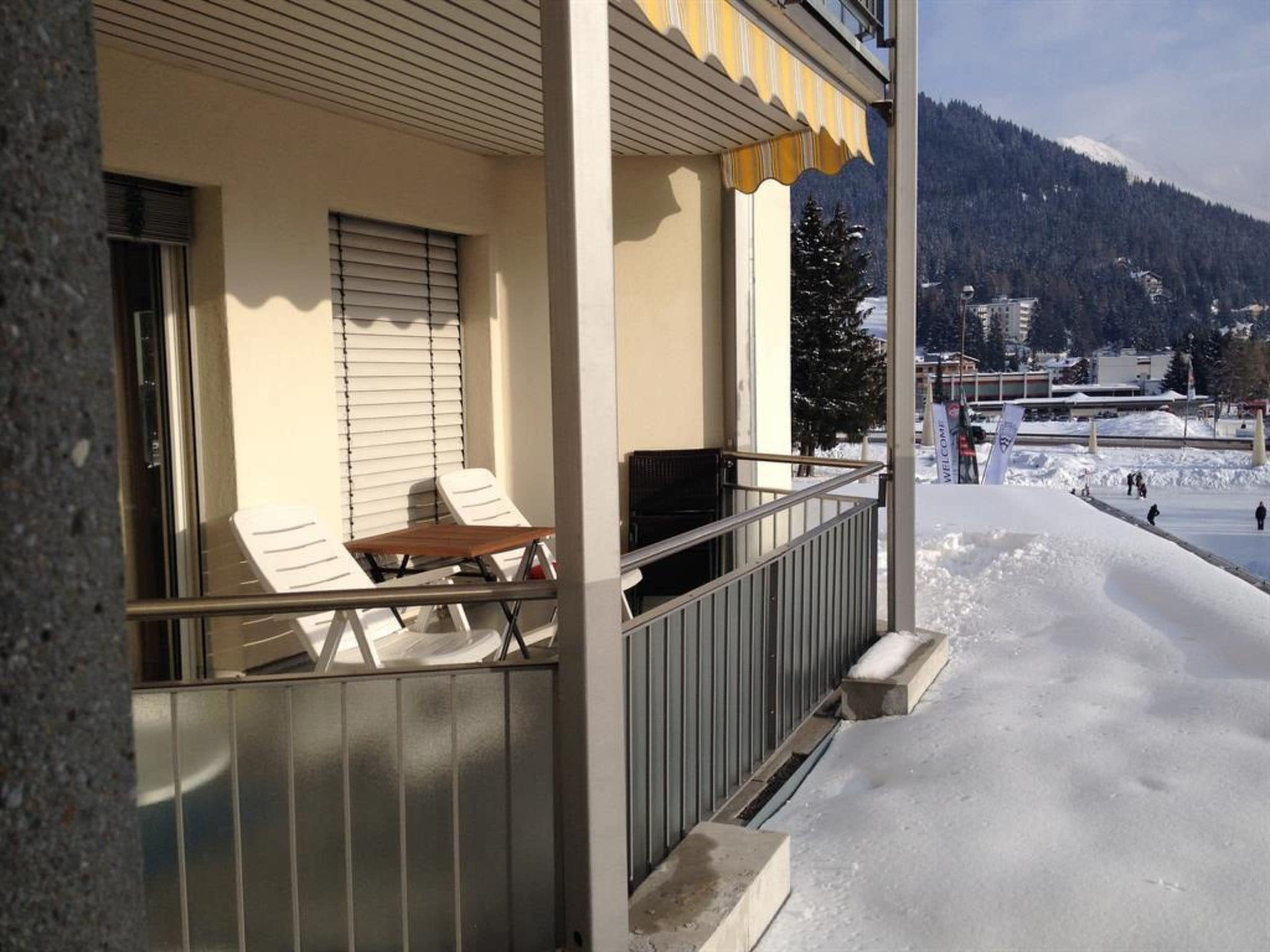 Ein Balkon mit Tisch und Stühlen, der auf eine verschneite Landschaft mit einem Berg im Hintergrund blickt.