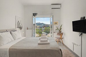 A bedroom with a bed, a TV, a potted plant, and a view of a cityscape. - Kalliopi's Apartment with Stunning Acropolis View (Athens)