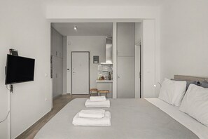 A modern hotel room with a large bed, a flat-screen TV mounted on the wall, a small kitchenette, and a door leading to a bathroom. - Kalliopi's Apartment with Stunning Acropolis View (Athens)