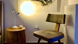 A room with a wooden side table, a chair, a wall-mounted lamp, and a radiator. - Kalliopi's Apartment with Stunning Acropolis View (Athens)