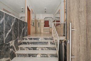 A marble staircase leading to a room with a wooden door and a red accent wall. - Kalliopi's Apartment with Stunning Acropolis View (Athens)