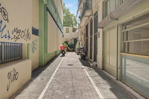 A narrow alleyway with a brick pavement, a motorbike parked on the right, and graffiti on the walls. - Kalliopi's Apartment with Stunning Acropolis View (Athens)