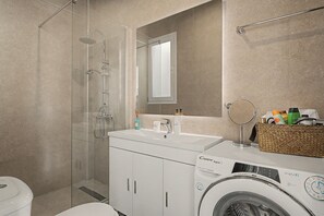 A modern bathroom with a glass-enclosed shower, a sink with a mirror, and a washing machine. - Kalliopi's Apartment with Stunning Acropolis View (Athens)