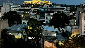 A cityscape with a prominent building illuminated in the background, a sign reading 'Sandro Parkson,' and a balcony railing with string lights. - Kalliopi's Apartment with Stunning Acropolis View (Athens)