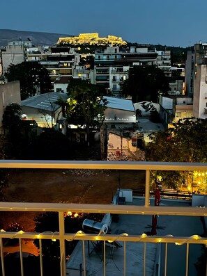 Paisagem urbana com um edifício em destaque iluminado ao fundo, uma placa com a inscrição 'Sandro Parkson' e um corrimão de varanda com luzes de cordão.