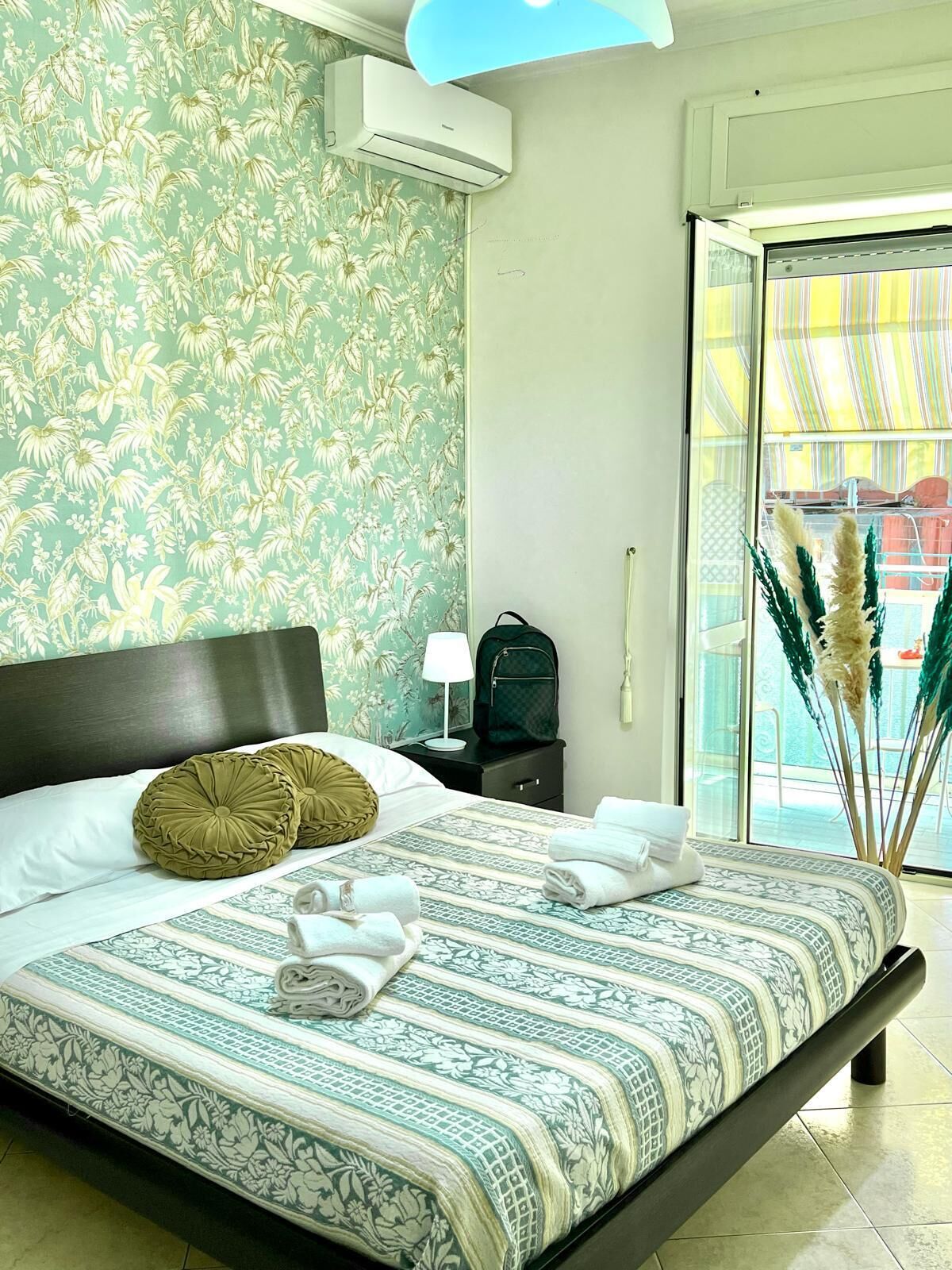 Une chambre d’hôtel avec un lit, une table de chevet, une lampe, une valise et une vue sur l’extérieur.