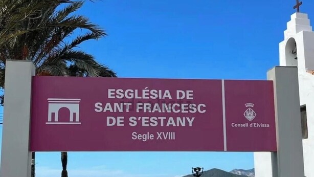 Schild für die Iglesia de Sant Francesc de S'Estany, 18. Jahrhundert, mit blauem Himmel und Palmen im Hintergrund.