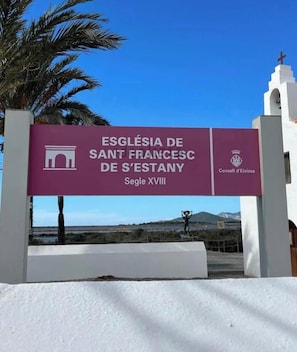 Opastekyltti, joka ohjaa Iglesia de Sant Francesc de S'Estany -kirkkoon, joka on rakennettu 1700-luvulla. Kyltistä avautuu selkeä näkymä ympäröivään maisemaan.