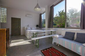 A modern room with a bed, a bench, a sofa, and large windows. - Ibiza | Salinas Garden Cottage | Sleeps 4 (Sant Josep de sa Talaia)