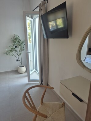 Ein Zimmer mit an der Wand montiertem Fernseher, einem Blumentopf, einem Stuhl und einem Fenster mit Vorhängen.