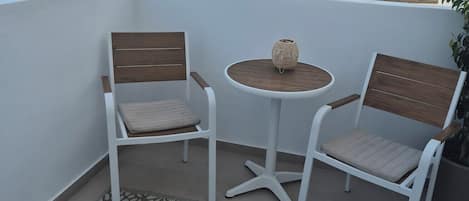 A balcony with two white chairs, a small round table, and a patterned rug.