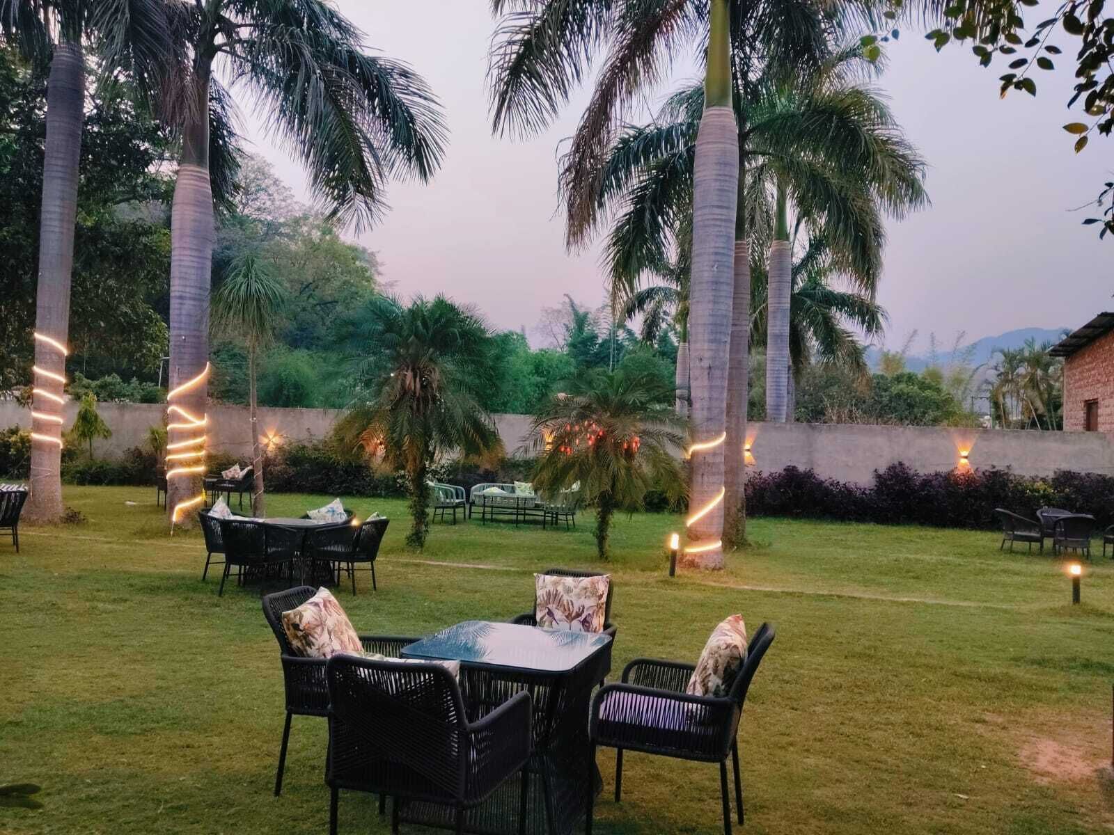An outdoor seating area with tables and chairs, surrounded by palm trees and a low wall.