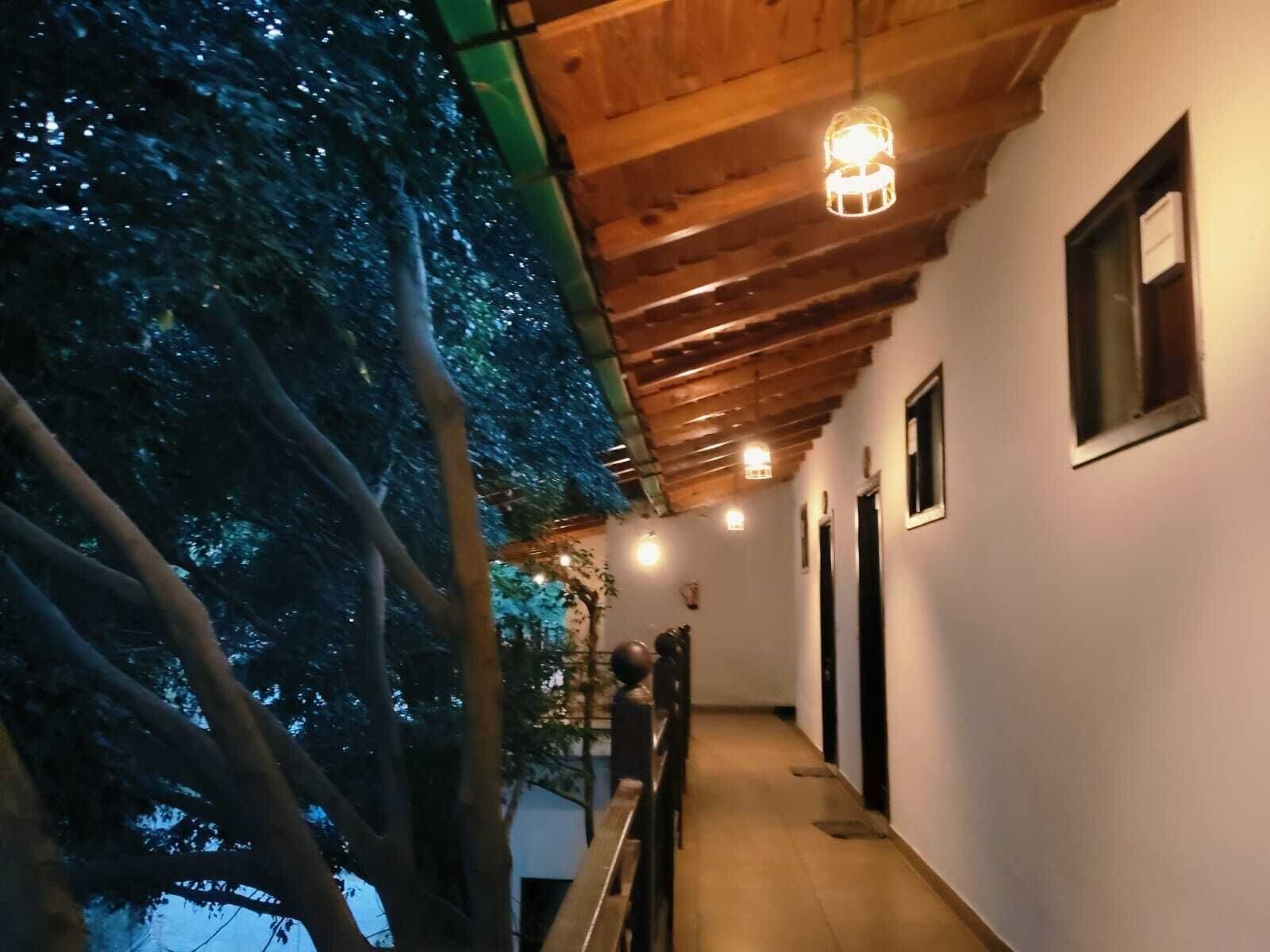 Pasillo con vigas de madera en el techo, barandilla y vista a árboles.