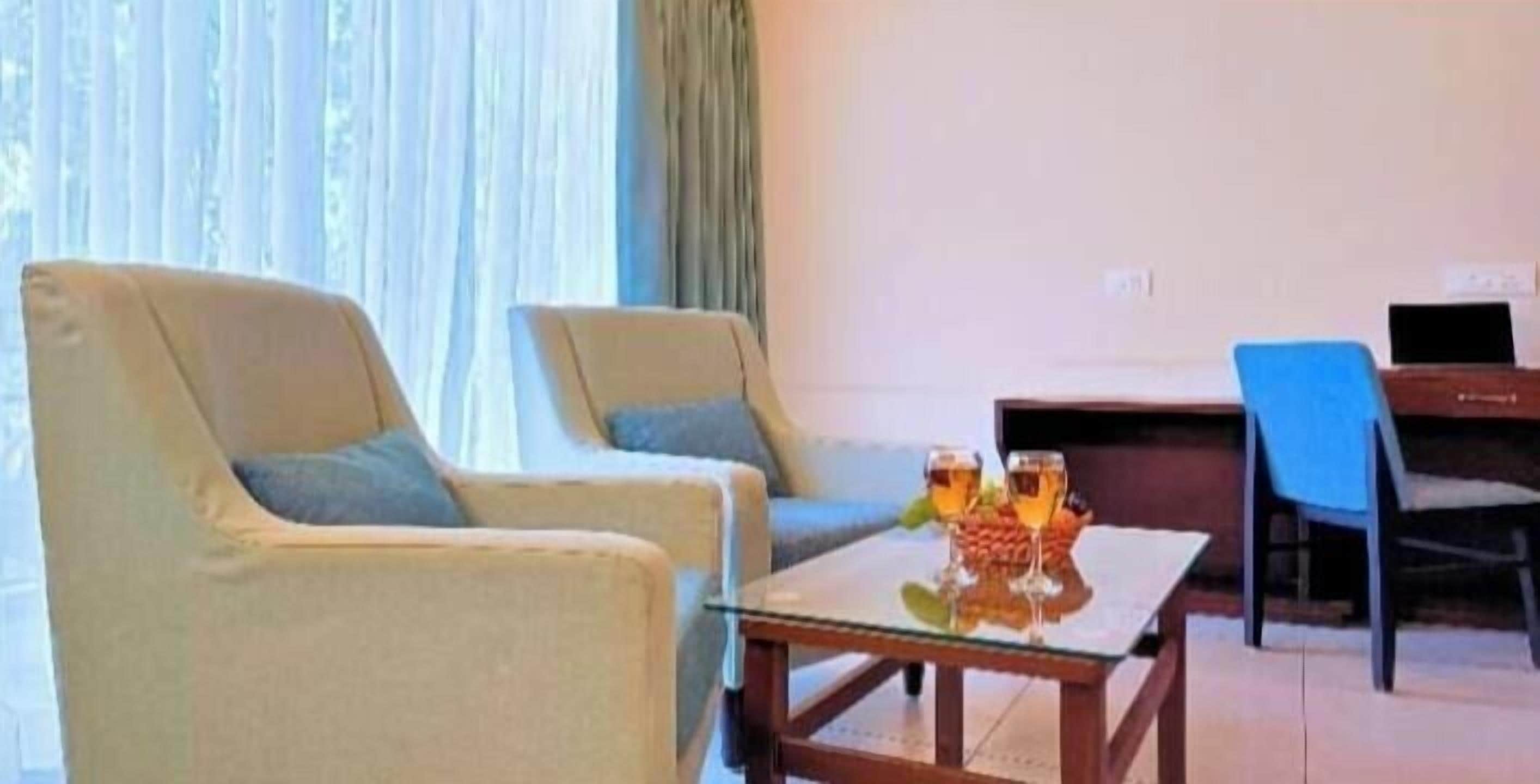 A room with two armchairs, a small table with a glass, and a laptop on a desk.