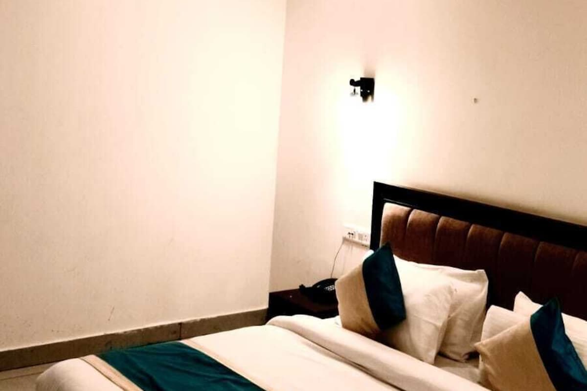 A bedroom with a wooden ceiling, a bed with pillows, a bedside table, and a wall-mounted light.
