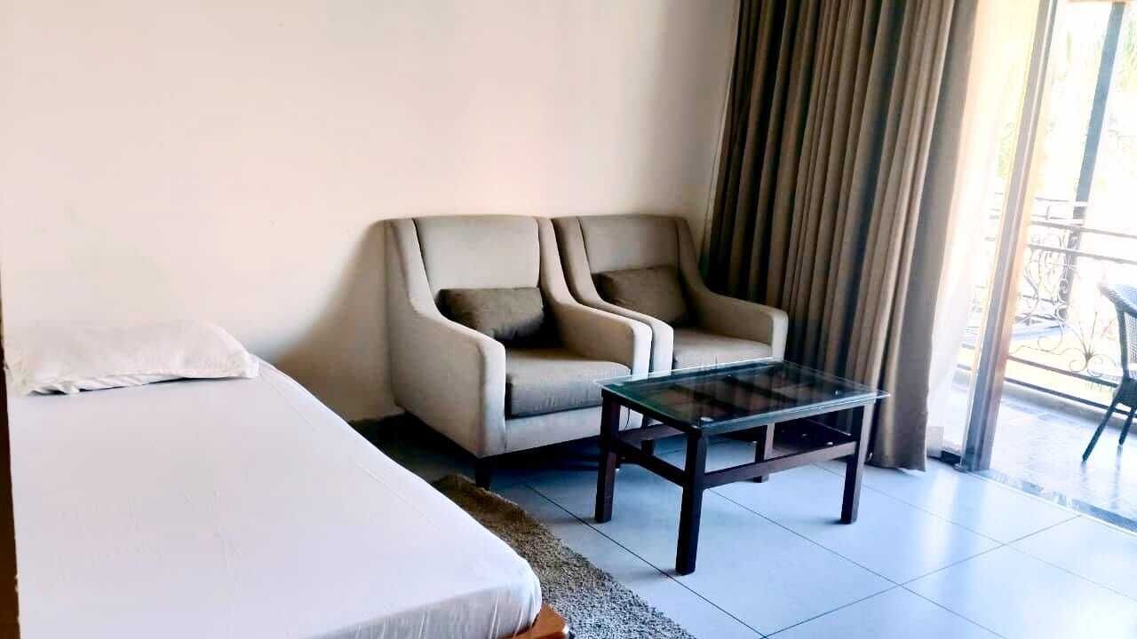 Habitación de hotel con cama, sofá, una mesita de centro de vidrio y vistas al exterior a través de una ventana con cortinas.